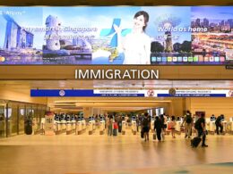 Large immigration hall at an airport with a row of self service kiosks and a prominent IMMIGRATION sign above travellers queuing