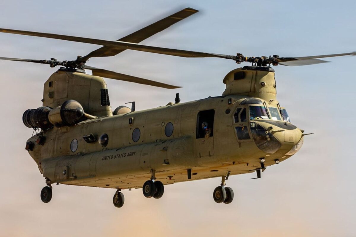 US Army awards Collins 2M Chinook modernization deal Twin rotor US Army helicopter Chinook in flight side view with open cabin and landing gear visible against a sunset sky