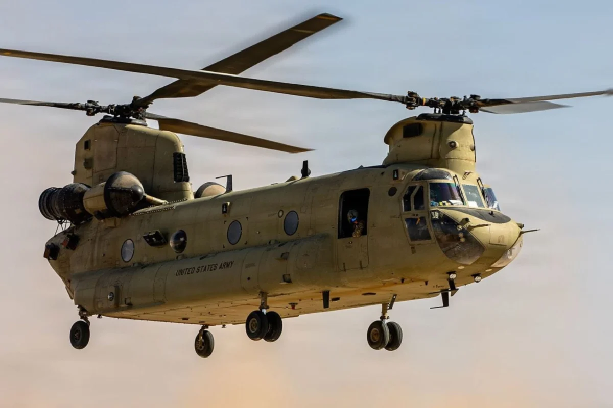US Army awards Collins 2M Chinook modernization deal Twin rotor US Army helicopter Chinook in flight side view with open cabin and landing gear visible against a sunset sky