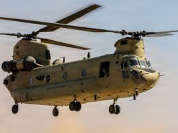 Twin rotor US Army helicopter Chinook in flight side view with open cabin and landing gear visible against a sunset sky