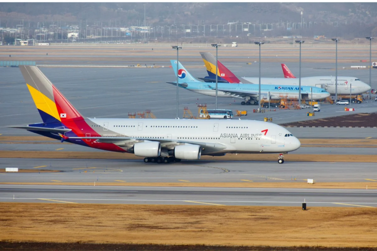 Korean Air Asiana secure approvals for December merger Wide view of an airport apron with multiple parked aircraft foreground features an Asiana Airlines jet with a colorful tail