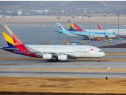 Wide view of an airport apron with multiple parked aircraft foreground features an Asiana Airlines jet with a colorful tail