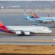 Wide view of an airport apron with multiple parked aircraft foreground features an Asiana Airlines jet with a colorful tail