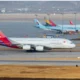 Wide view of an airport apron with multiple parked aircraft foreground features an Asiana Airlines jet with a colorful tail