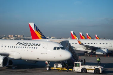 Several Philippine Airlines planes parked at the gate displaying red blue and yellow sunburst tail logos