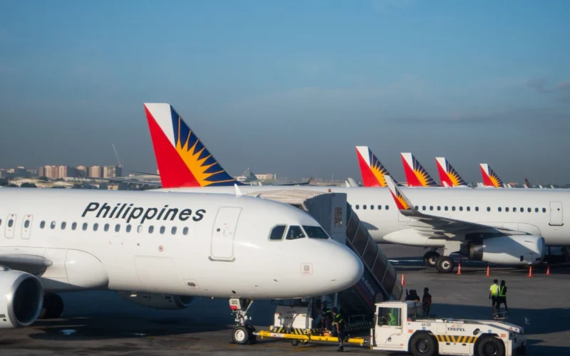 Several Philippine Airlines planes parked at the gate displaying red blue and yellow sunburst tail logos