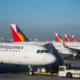 Several Philippine Airlines planes parked at the gate displaying red blue and yellow sunburst tail logos