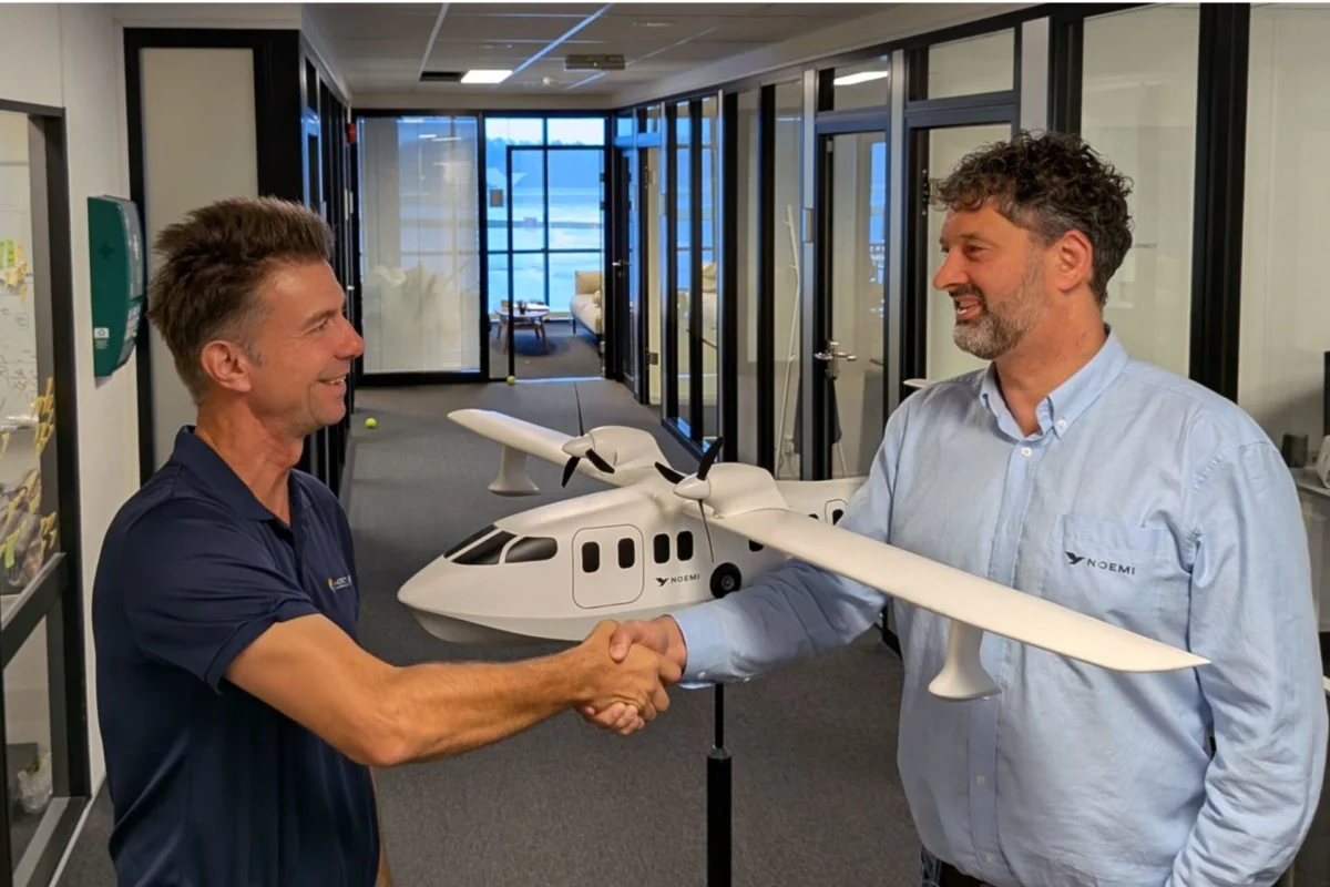 NOEMI Aerospace signs seaplane deals in India Philippines Two men shake hands in a hallway with a white model airplane between them smiling at each other in an office setting