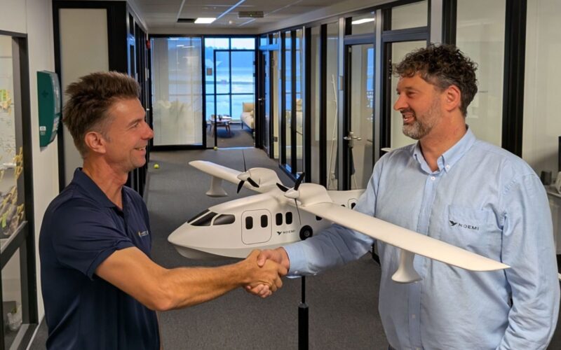NOEMI Aerospace signs seaplane deals in India Philippines Two men shake hands in a hallway with a white model airplane between them smiling at each other in an office setting