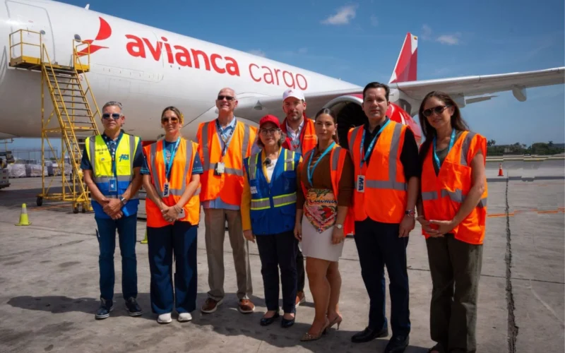 Group of airport workers in orange vests posing in front of an Avianca Cargo plane on the tarmac