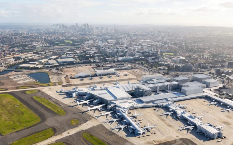 Aerial view of a large airport terminal with many airplanes parked at gates and a distant city skyline in the background
