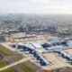 Aerial view of a large airport terminal with many airplanes parked at gates and a distant city skyline in the background