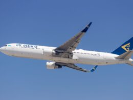Air Astana passenger jet in flight with a blue tail and yellow emblem against a clear blue sky wings extended