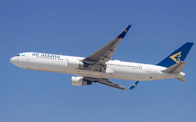 Air Astana passenger jet in flight with a blue tail and yellow emblem against a clear blue sky wings extended