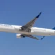 Air Astana passenger jet in flight with a blue tail and yellow emblem against a clear blue sky wings extended