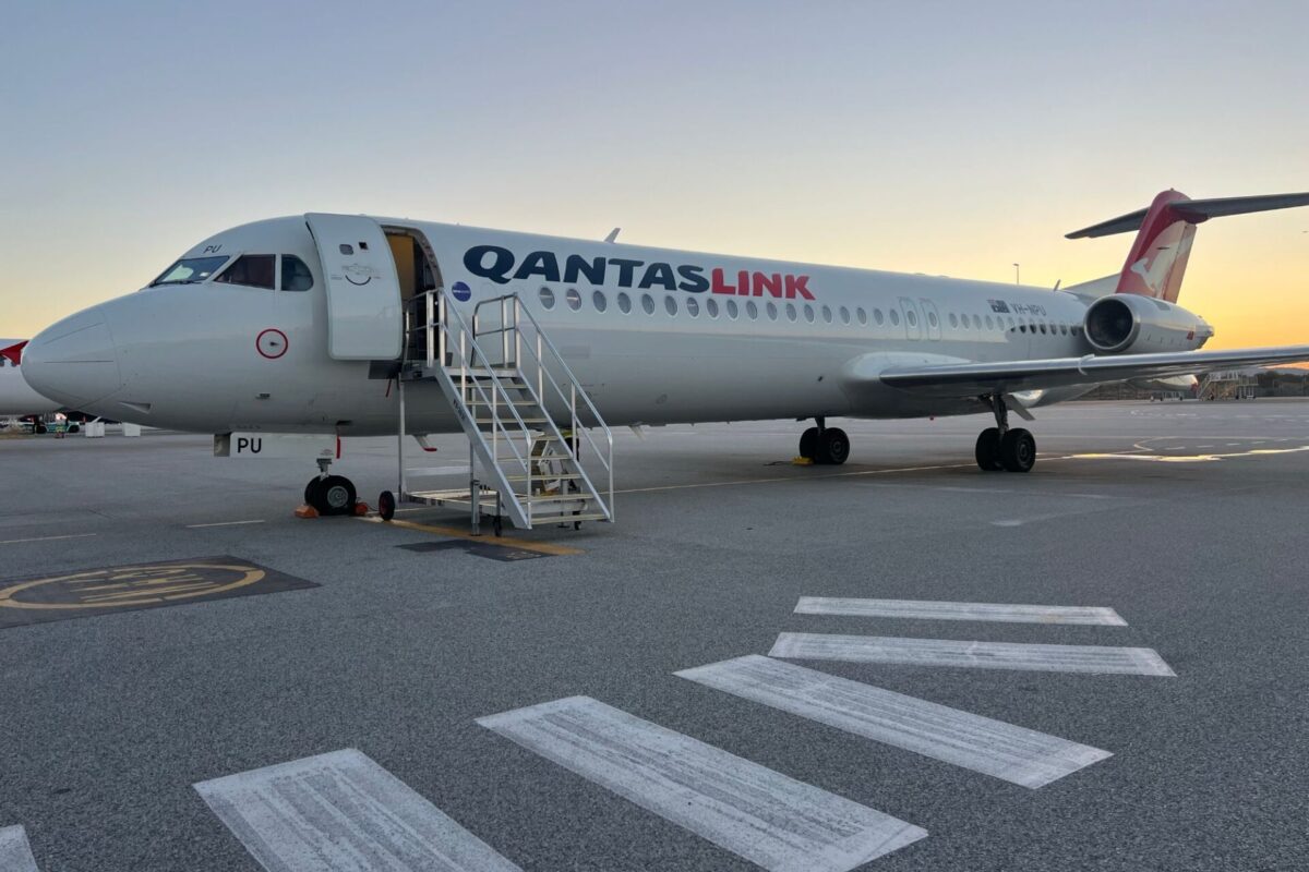 QantasLink airliner parked at the gate with mobile stairs attached at sunset