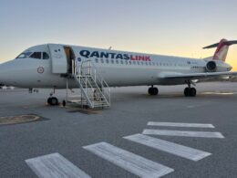QantasLink airliner parked at the gate with mobile stairs attached at sunset