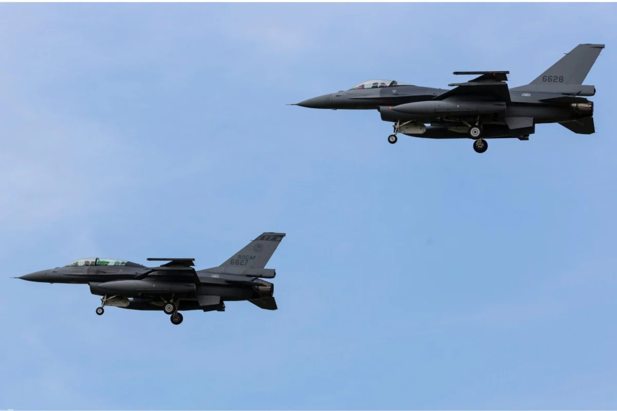 Three gray fighter jets in formation mid flight against a clear blue sky their landing gears down as they pass overhead