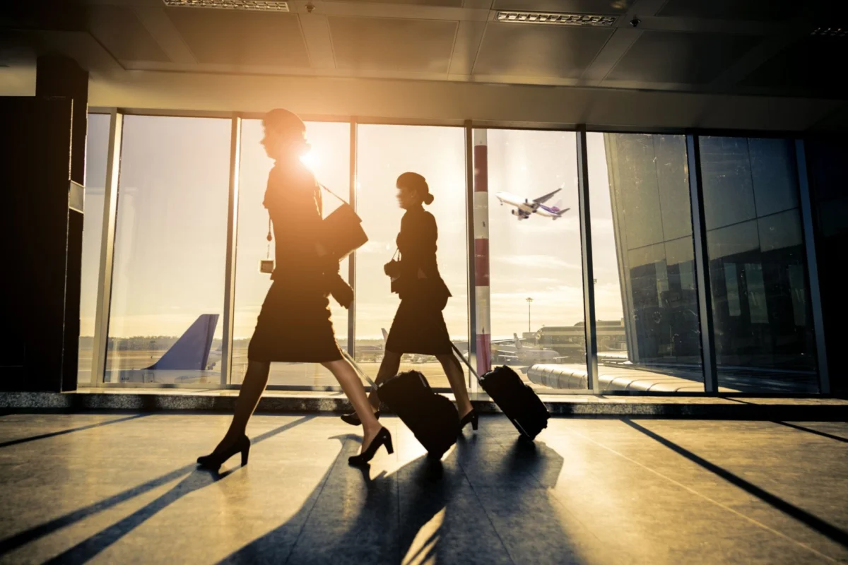 Flight crew face highest radiation cancer risk study Two silhouette women walking with rolling suitcases through an airport concourse at sunset large glass windows behind them