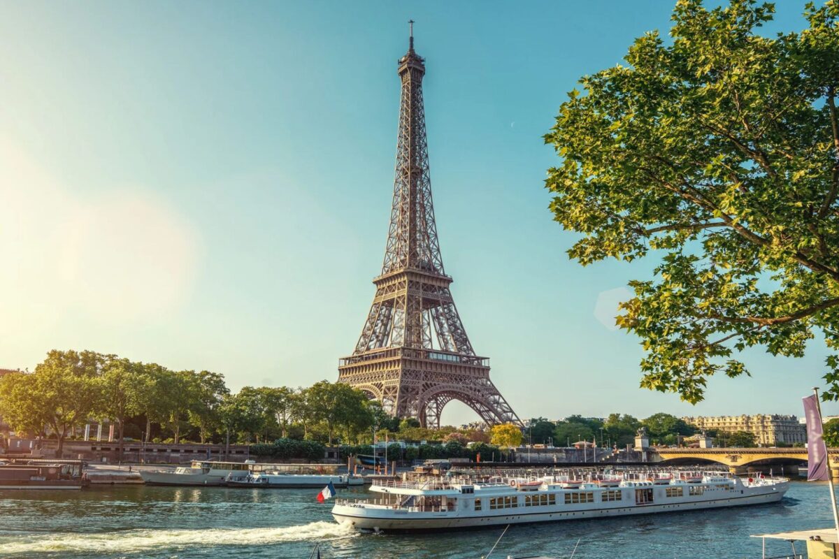 Eiffel Tower along the Seine with boats on the river and green trees on a sunny day in Paris