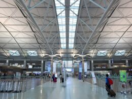 Wide view of a spacious airport terminal with a geometric steel beam ceiling skylight panels and travelers with luggage in the foreground