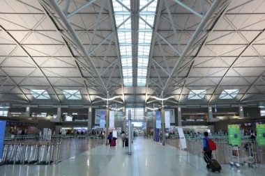 Wide view of a spacious airport terminal with a geometric steel beam ceiling skylight panels and travelers with luggage in the foreground