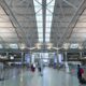 Wide view of a spacious airport terminal with a geometric steel beam ceiling skylight panels and travelers with luggage in the foreground