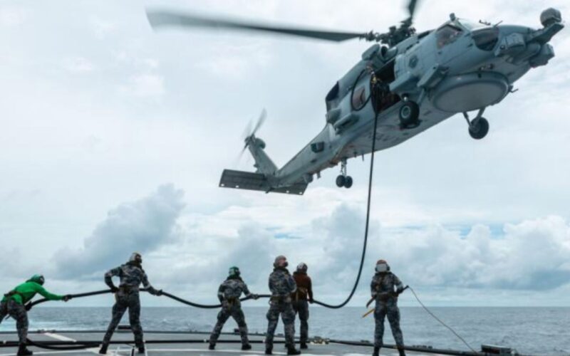 ADF RAAF roll out low carbon fuel blends nationwide Military helicopter hovers above a ship deck lowering a rescue line to sailors preparing to hoist