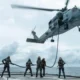 Military helicopter hovers above a ship deck lowering a rescue line to sailors preparing to hoist