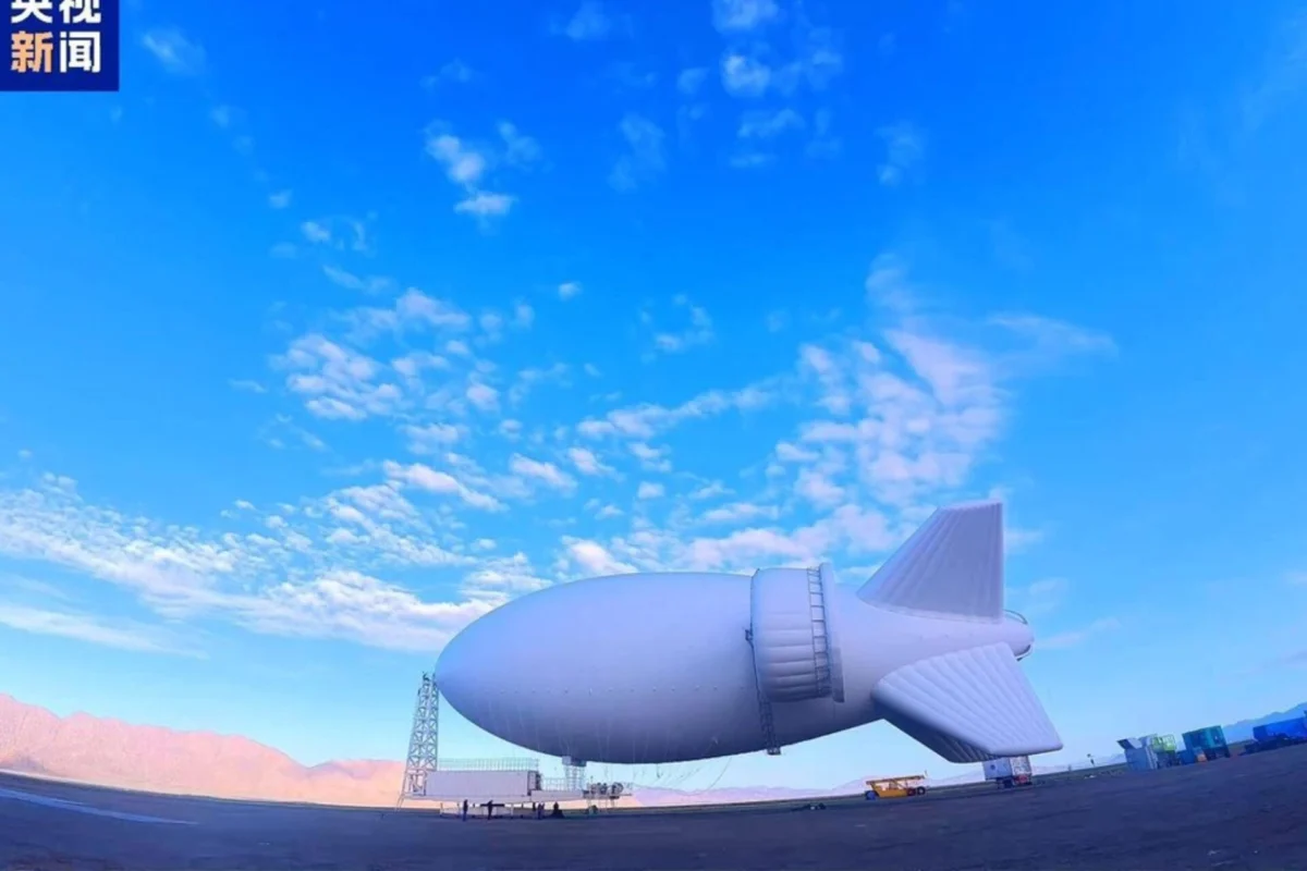 Huge white airship hovering over an airfield with mountains in the distance Chinese news logo in the top left corner