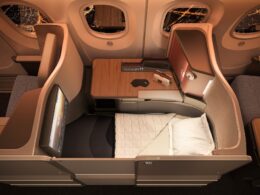 Business class flatbed seat in an airplane with a wooden table window views and a padded bed setup for rest