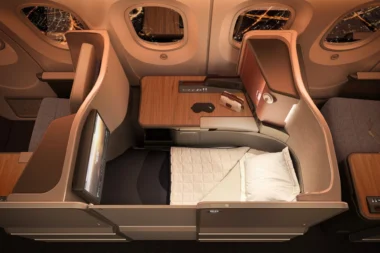 Business class flatbed seat in an airplane with a wooden table window views and a padded bed setup for rest