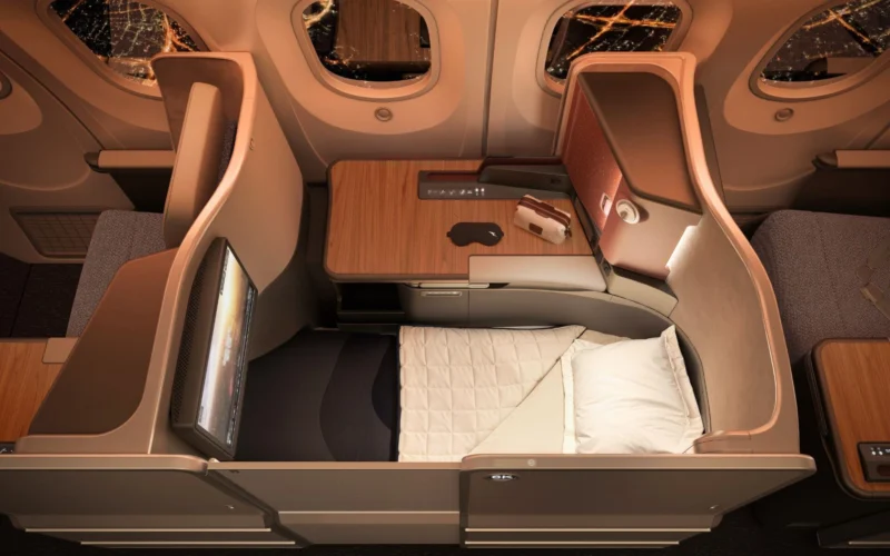 Business class flatbed seat in an airplane with a wooden table window views and a padded bed setup for rest