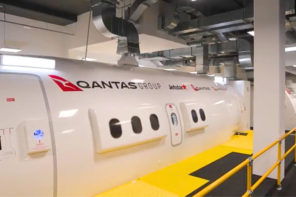 Qantas opens M flagship crew training center in Sydney Side view of a white Qantas Group aircraft in a hangar with logos for Qantas and Jetstar visible along a yellow maintenance walkway