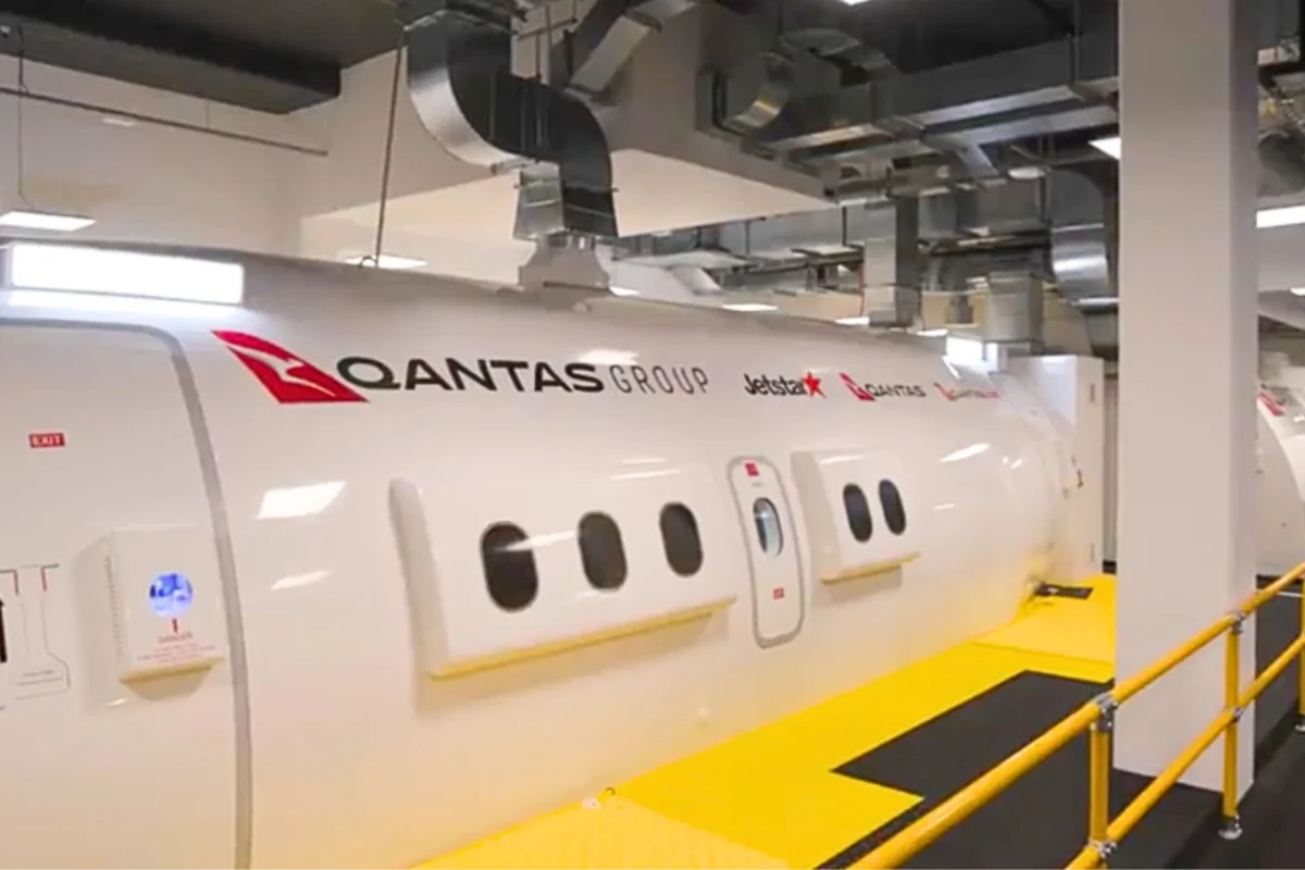 Side view of a white Qantas Group aircraft in a hangar with logos for Qantas and Jetstar visible along a yellow maintenance walkway