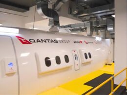 Side view of a white Qantas Group aircraft in a hangar with logos for Qantas and Jetstar visible along a yellow maintenance walkway