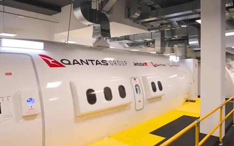Qantas opens M flagship crew training center in Sydney Side view of a white Qantas Group aircraft in a hangar with logos for Qantas and Jetstar visible along a yellow maintenance walkway
