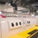 Side view of a white Qantas Group aircraft in a hangar with logos for Qantas and Jetstar visible along a yellow maintenance walkway