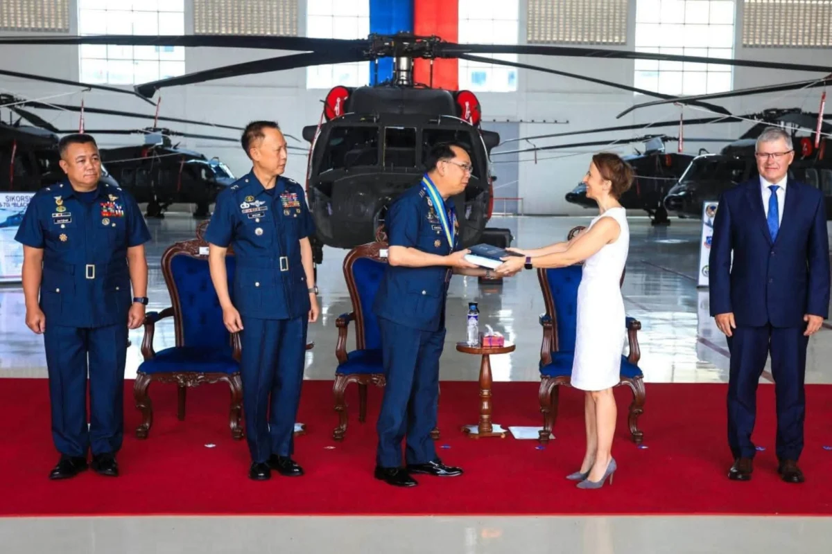 Philippine Air Force completes 32 unit Black Hawk delivery Officials in military uniforms and a woman in a white dress exchange a book in a helicopter hangar with a red carpet backdrop