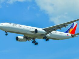 Philippine Airlines wide body airliner in the sky with landing gear extended against a blue backdrop tailfin visible with colorful logo