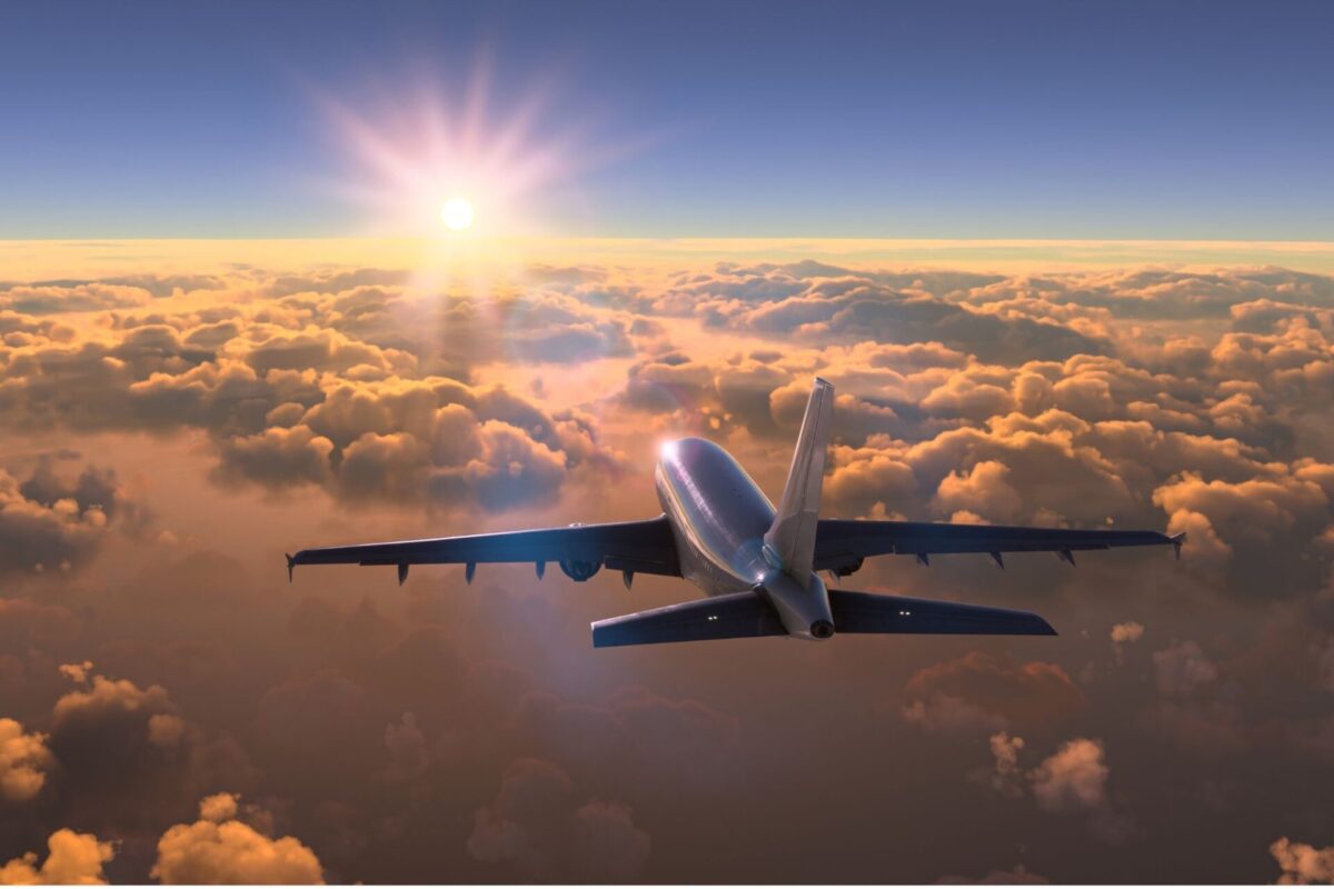 Airplane wing seen from the cabin window flying above sunlit clouds at sunrise in a golden sky