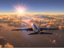 Airplane wing seen from the cabin window flying above sunlit clouds at sunrise in a golden sky
