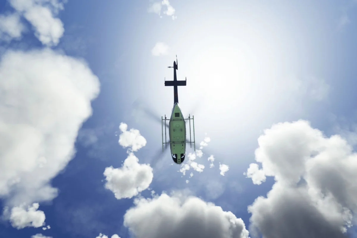 Two killed as firefighting helicopters collide in Greece Green helicopter photographed from below against a bright sun and scattered clouds in a blue sky view from beneath the aircraft