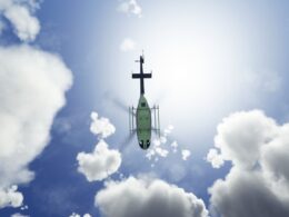 Green helicopter photographed from below against a bright sun and scattered clouds in a blue sky view from beneath the aircraft