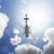 Green helicopter photographed from below against a bright sun and scattered clouds in a blue sky view from beneath the aircraft