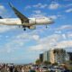 Air Astana Airbus A320neo flying low over a crowded beachfront with people watching and cars parked along the promenade city buildings in the background