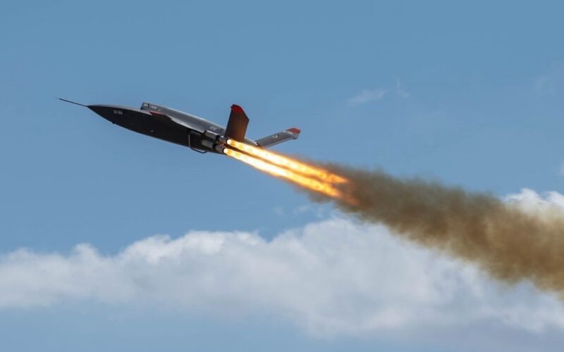 Valk Takeoff Hero Military jet flying left to right with orange afterburner flames and a smoky trail against a blue sky in flight