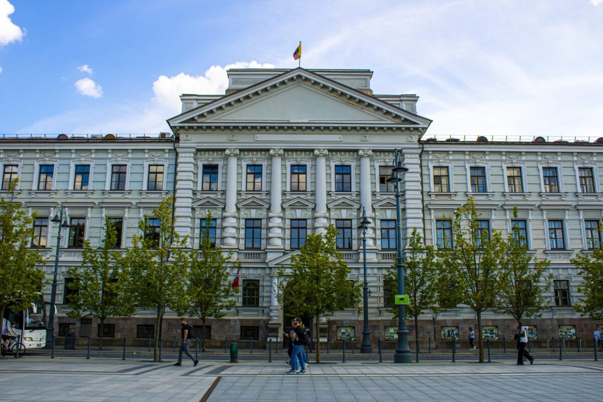 Vilnius Regional Court Lithuania Neoclassical building facade with columns and triangular pediment flag on top blue sky trees lining the street pedestrians on the sidewalk