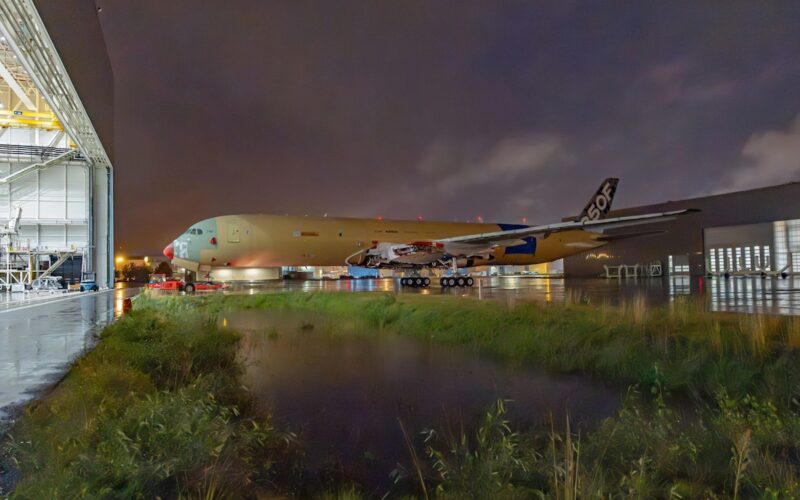 a350f Wide body aircraft on the tarmac beside an open hangar at night with ground support equipment and a wet reflective surface nearby