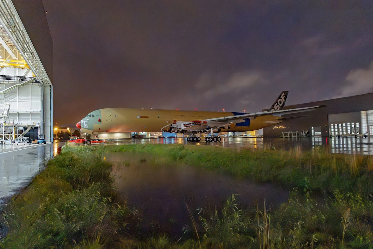 a350f Wide body aircraft on the tarmac beside an open hangar at night with ground support equipment and a wet reflective surface nearby